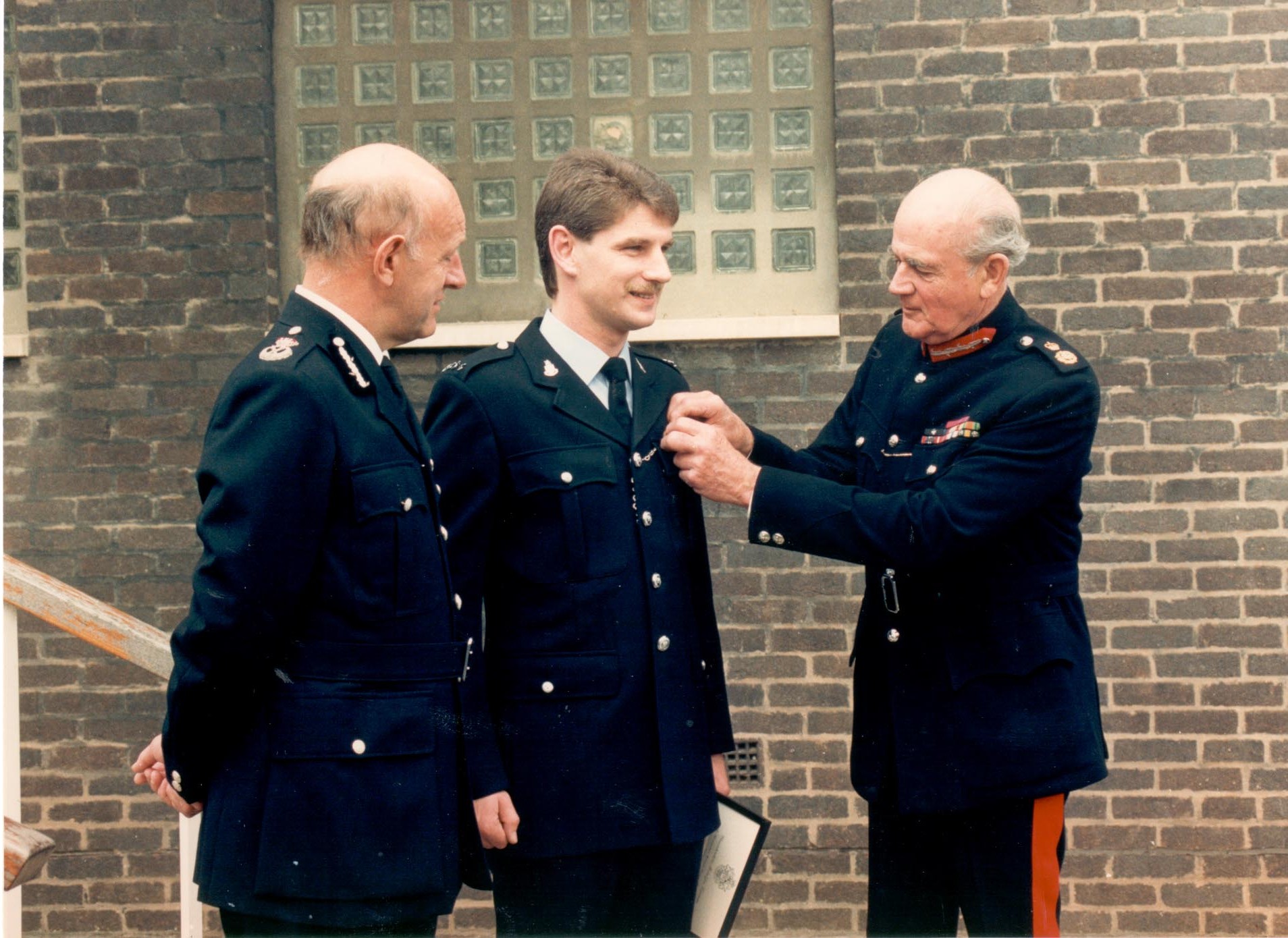 Presentation of Queen's award for Brave Conduct as a result of the 1987 Gloucester Police Station Siege. Police Constable Bill Matthews ( Bamfurlong) receiving his award from the County Lord Lieutenant Colonel Martin Gibbs with Chief Constable Albert Pacey. (Gloucestershire Police Archives URN 484) 